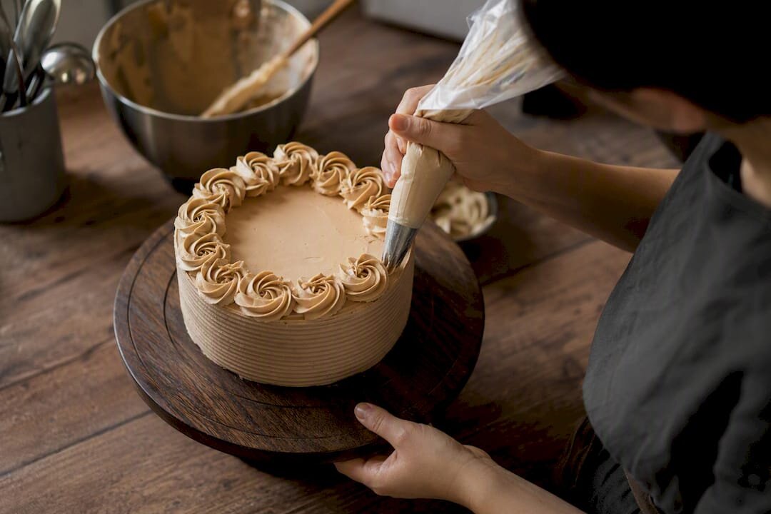 Mani che decorano una torta con delle rosette su un piatto girevole